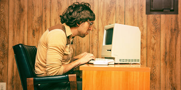Homme assis devant un vieil ordinateur dans un décor rétro
