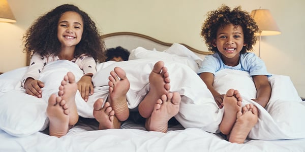 Pieds qui ressortent des couvertures dans un lit avec enfants souriants