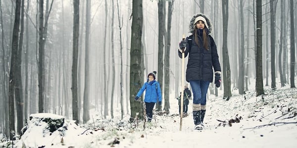 Enfants avec vêtements d'hiver et bâton qui marchent dans une forêt enneigée