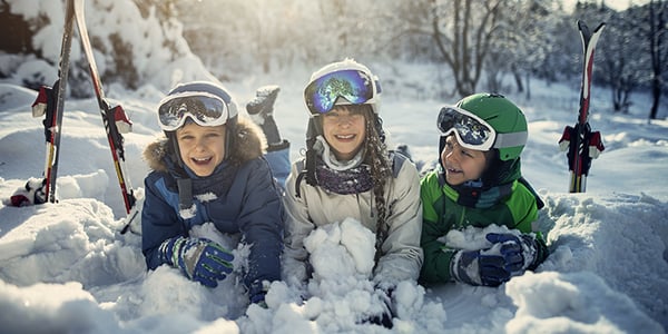 3 enfants avec lunettes de ski couchés dans la neige