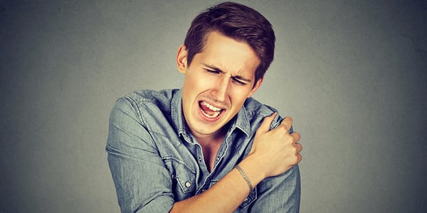 Homme qui tient son épaule avec une expression de douleur sur le visage