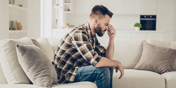 Homme assis sur sofa les yeux fermés qui tient sa tête