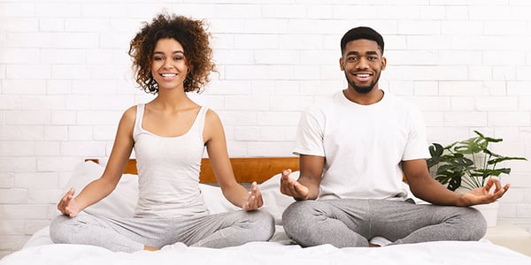 Femme et homme assis dans la position du lotus sur un lit