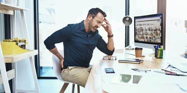 Homme assise sur une chaise devant un ordinateur qui tient le bas de son dos