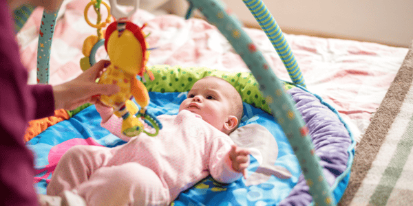 bébé couché sur le dos sur un tapis d'éveil qui regarde un jouet