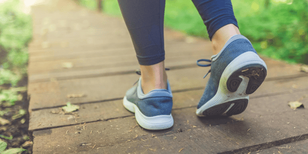 Jambes d'une personne en vêtements et chaussures de sport qui marche sur un trottoir en bois