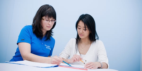 Thérapeute avec polo PhysioExtra qui pointe quelque chose sur une feuille à une femme