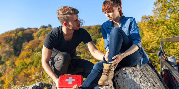 Homme avec trousse de premiers soins qui porte assistance à une femme qui tient sa cheville