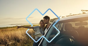 couple on a road trip checking a paper map next to parked car with ocean view at sunset
