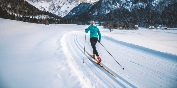 Femme de dos en ski de fond sur un terrain plat enneigé avec montagnes au loin