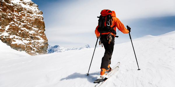 Personne qui grimpe une montagne enneigée avec ski et bâtons