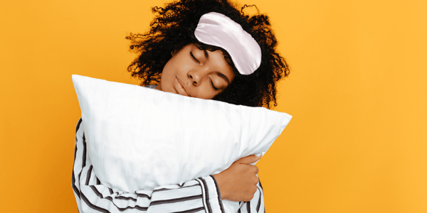 Femme en pyjama qui tient un oreiller dans ses bras les yeux fermés