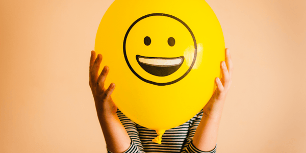 Visage souriant dessiné sur un ballon tenu par une personne devant son visage